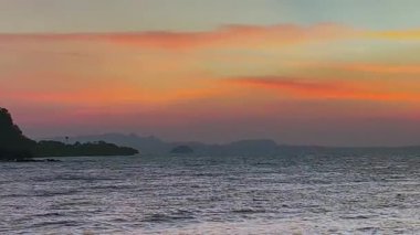 Sakin kıyı sularının üzerinde gün batımı yumuşak dalgalar ve renkli gökyüzü. Seyahat reklamları, gevşeme temaları ya da video geçmişleri için ideal. Huzuru, doğayı ve kaçışı çağrıştırır..