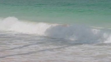 Köpüklü okyanus dalgaları kıyıya vuruyor ritmik hareketlerle, güneş ışığı mavi-yeşil su güzelliğinde parıldıyor video arkaplanları veya reklamlar için..