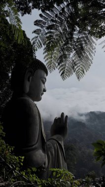 Bereketli orman yaprakları ve sisli dağlarla çevrili huzurlu bir Buda heykeli.
