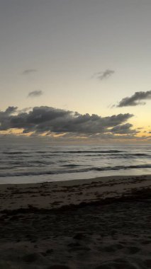 Gün batımında sakin suyu ve bulutlu gökyüzü olan huzurlu bir sahil manzarası..