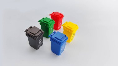 Gri yüzeylerdeki farklı organize düzende gösterilen çok renkli geri dönüşüm kutuları. Çevre eğitimi, atık ayırma görselleri ve geri dönüşüme odaklı çevre farkındalığı kampanyaları için ideal