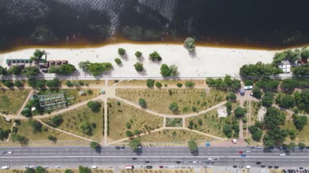 Vista aérea del parque de la ciudad con árboles verdes, playa y río por la carretera — Vídeo de stock