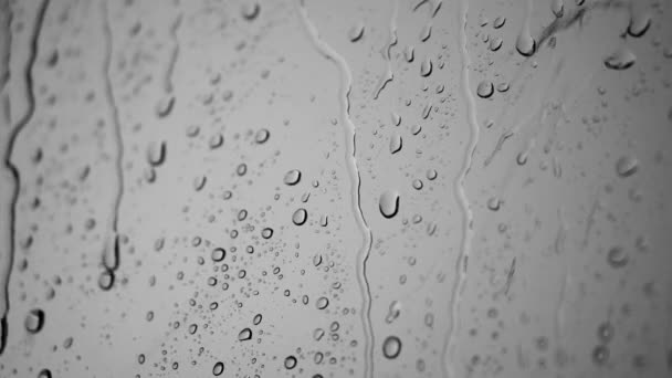 Gotas de lluvia goteando en un cristal de ventana. Viento fuerte. Fondo blanco y negro — Vídeos de Stock