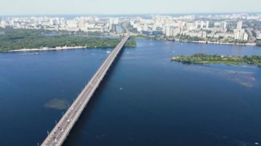 Gökdelenleri ve arabaları olan büyük şehir manzarası nehirde bir köprüye biniyor.