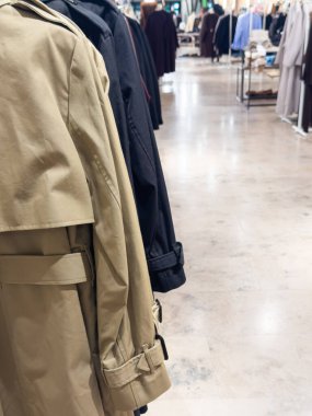Classic beige trench coat and other outerwear hanging in a stylish mass market store. Represents trendy autumn fashion and modern retail environment. 