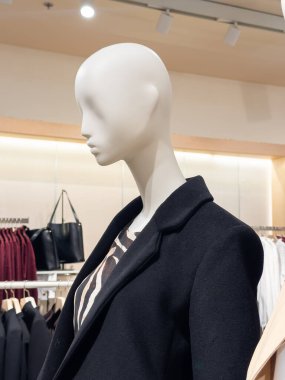 Stylish mannequin showcasing a modern autumn-winter fashion look with a black coat and animal print top. Highlights contemporary trends in retail display. Vertical photo. 