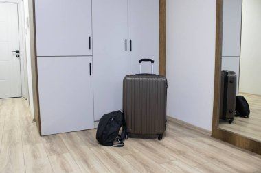 Parlak bir apartman koridoru. Dolabın yanında yuvarlanan bir bavul ve sırt çantası ve uzun bir ayna. Varış teması kontrol, kısa vadeli kiralama, iş ya da boş zaman ziyareti.