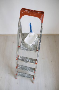 Boya tepsisi ve fırça tutan metal merdiven platformunun yukarıdan görünüşü duvar boyası ve ev dekorasyonunu gösteriyor..