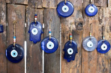 Kırsal bir ahşap çitte asılı mavi cam nazar ve hamsa muskaları. Geleneksel Türk koruma sembolleri; zanaatkar el sanatları ve seyahat dekorasyonu kavramı.