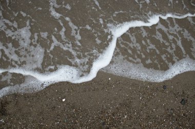 Daha koyu kumların üzerinde kıvrımlı köpük bandı. Seyahat, sağlık, kaplıca ve tasarım kullanımı için kopya alanı olan yüksek kontrast minimal deniz kıyısı dokusu.