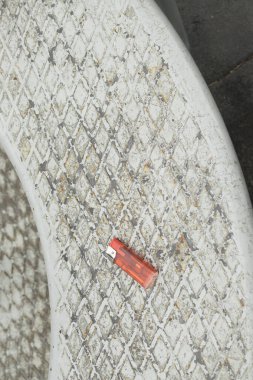 Yıpranmış bir elmas plaka yüzeyindeki kayıp kırmızı plastik çakmağa yakın çekim. Kavram: çöplük, sigara alışkanlığı, kentsel kirlilik, risk ve kamu alanlarında güvenlik.