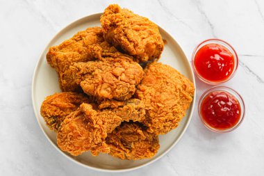 Yuvarlak beyaz bir tabakta kızartılmış tavukların servis edildiği tepeden bakıldığında, mermer bir yüzey üzerinde iki küçük cam sosla eşleştirilmiş..