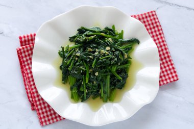 Kızarmış ıspanakla dolu beyaz bir tabak ve hafif soslu doğranmış sarımsak..