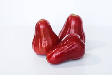 Temiz beyaz arka planda, gül elması ya da balmumu elma olarak da bilinen taze jambu hava kümesi meyvenin çan şeklini ve parlak kırmızı derisini gözler önüne seriyor..