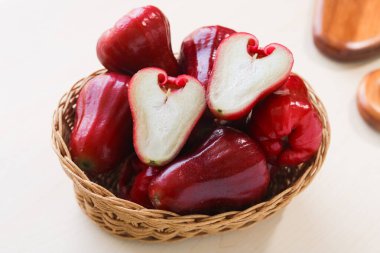 Bir sepet taze Jambu Air (Su, Gül, Balmumu Elma), hafif ahşap arka planda taze, beyaz etini göstermek için ikiye bölünmüş bir meyve ile.