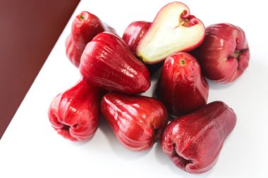 Bir yığın taze Jambu Air (Su, Gül, Balmumu elması), beyaz ve kestane rengi arka planda taze beyaz etini göstermek için ikiye bölünmüş bir meyve ile.