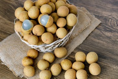 Şeffaf beyaz eti ortaya çıkarmak için iki meyve soyulmuş, dokuma sepetinde büyük bir longan (kelengkeng) meyvesi yığını.