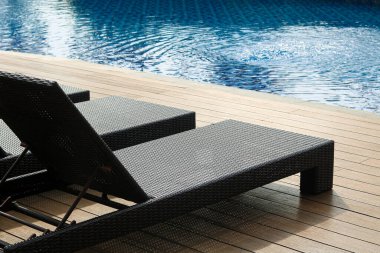 Sakin, mavi suyu olan bir yüzme havuzu ve ahşap bir güvertede şık şezlonglar, rahatlamak için mükemmel bir atmosfer yaratıyor..