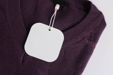 Koyu mor bir elbisede asılı beyaz yuvarlak kenarlı kare etiketli, metin veya logo için geniş bir kopya alanı olan yakın plan bir fotoğraf..