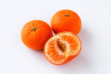 İki tam mandalina portakalı ve bir yarısı soyulmuş, parlak turuncu rengi ve sulu bölümleri beyaz arka planda sergiliyorlar..