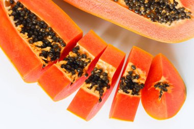 Taze bir papaya, ikiye bölünmüş ve ön planda çeşitli dilimlerle, meyvenin canlı portakal eti ve siyah tohumlarını sergiliyor..