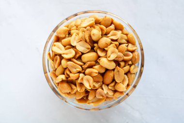 Fırında pişmiş fıstıklarla dolu cam bir kasenin üst görüntüsü, koyu kahverengi rengini ve kavrulmuş dokusunu vurguluyor..