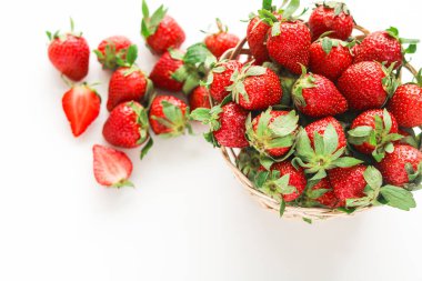 Beyaz arka planda olgun, kırmızı çileklerle dolu bir hasır sepet. Birkaç çilek serpilmiş ve sepetin yanına yarıya bölünmüş..