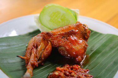 Ayam Bakar (Endonezya Izgara Tavuğu), kırmızımsı kahverengi salamura. Beyaz bir tabakta servis edilir ve yanında sambal (acı biber ezmesi) ve salatalık ve lahana dilimleri ile birlikte.. 