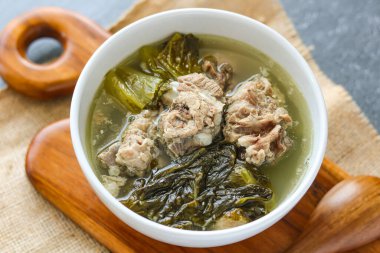 Bak Kut 'un sıcak bir kâsesine yakın çekim koyu gri arka planda servis edildi. Lezzetli et çorbası yumuşak domuz kaburgası ve büyük yeşil yapraklı sebze parçaları içerir..