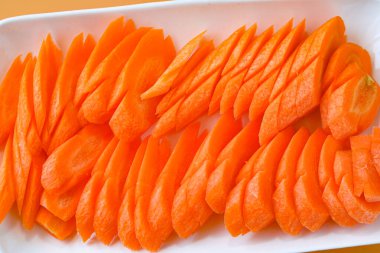 İnce dilimlenmiş taze turuncu havuç, beyaz bir tabakta düzgünce dizilmiş..