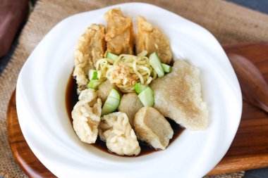 Bir tabak dolusu Pempek (ya da Empek-Empek), Palembang 'tan geleneksel bir Endonezya balık köftesi tabağı, erişte ve dilimlenmiş salatalıklı. Tabak koyu bir Cuko sosuna bulanmış..