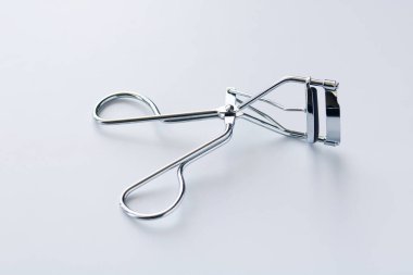 Gümüş rengi bir kirpik bigudisi, beyaz bir arka planda, göz makyajını geliştirmek için yaygın bir güzellik aracı.. 