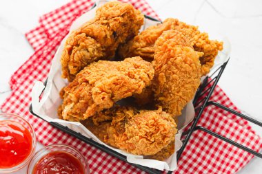 Kızarmış tavuk parçalarıyla dolu bir sepetin yakın görüntüsü, desenli altın-kahverengi kaplamalarını sergiliyor, kareli bir arka planda sosla servis ediliyor..