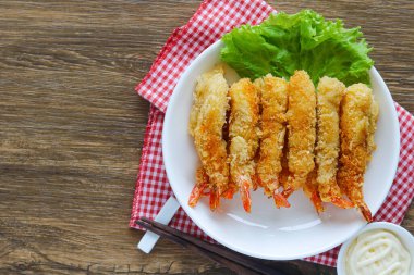 Kızarmış karides tabağının üst görüntüsü (Ebi Fry veya Tempura), taze marulla süslenmiş ve kırmızı kareli peçeteyle beyaz bir tabakta servis edilmektedir. Yanında yemek çubukları ve sosu var..