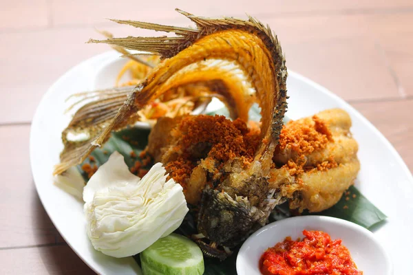Popüler bir Endonezya yemeği olan kızarmış Gourami 'ye (Gurame Goreng) yakın plan. Çıtır çıtır kırıntılar serpiştirilmiş ve yanında taze lahana, salatalık dilimleri ve ateşli kırmızı bir sambal ya da sambel var..