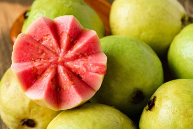 Yeşil guava meyvesinin tamamının yakın plan aranjmanı, canlı pembe bir iç mekan ortaya koyan yarım yamalak bir parça içeriyor. Et, dokusunu ve rengini vurgulamak için ustalıkla oyulmuştur..