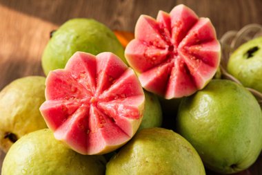 Yeşil guava meyvesinden oluşan bir düzenleme, göz kamaştırıcı derecede canlı pembe bir iç mekan ortaya çıkaran iki yarıyı vurguluyor. Et, dokuyu ve rengi göstermek için sanatsal olarak oyulmuştur..