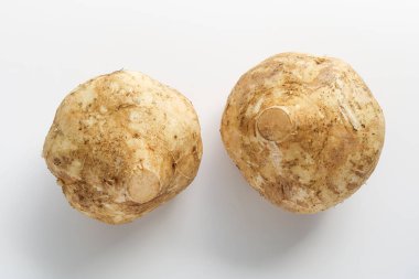 İki tam Bengkuang (Jicama), sert, kahverengi deriyi sergiliyor. Bu sebze, salata ve meyve hazırlıklarında sıkça çiğ yenir..