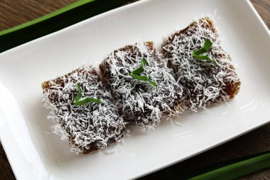 Beyaz dikdörtgen bir tabakta düzgünce dizilmiş üç parça ongol-ongol. Her parça, ahşap bir zemine dayanan parçalanmış hindistan ceviziyle cömertçe kaplanmış..