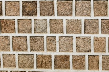 Kahverengi taştan bir duvarın tam kare arka planı taşın pürüzlü, gözenekli dokusunu ve zıt beyaz harcı gözler önüne seriyor..