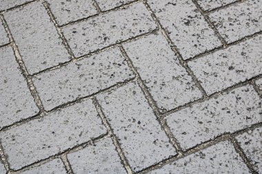 Geometrik desende birbirine kenetlenmiş gri tuğlaları olan asfalt bir yüzeyin tam çerçevesi.