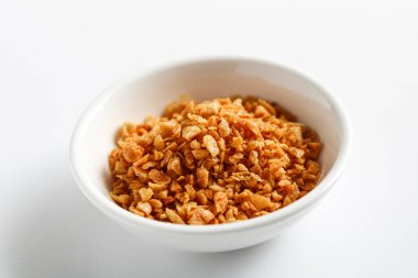 A view of golden-brown fried garlic bits in a small white bowl. These crispy, aromatic garlic flakes are a popular savory garnish for Asian soups, noodles, and rice dishes.