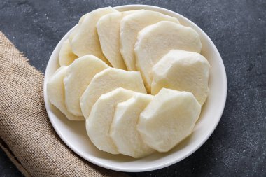 Kalın, soyulmuş beyaz dilimler, ham Jicama, Bengkuang olarak da bilinir, beyaz bir tabakta dizilmiştir. Çıtır çıtır, tatlı dilimler atıştırmalık ya da salata malzemesi olarak yemek için hazır..