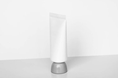 Temiz, minimalist kozmetik tüp matte beyazında, açık arkaplan üzerinde gri bir tabanda duruyor. El kremi, losyon, yüz yıkama veya diğer ürünler için ideal.