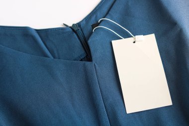 Koyu mavi bir elbiseye asılan minimalist bir etiket. Bu resim markalaşma, logo tasarımları veya moda ürünleri için ürün fiyatlandırması için mükemmeldir..