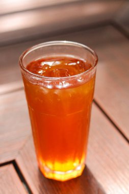 Sıcak ahşap yüzeyde ferahlatıcı bir bardak buzlu çay. Sıcak hava için serin bir içecek. Doğal ışıkla yakalanan.