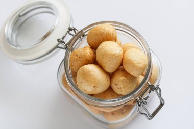 Beyaz arkaplanda küçük yuvarlak karides krakerleriyle (kerupuk udang) dolu bir kavanozun üst görünümü.