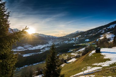 A breathtaking winter sunset near Kaprun, Austria, bathes the snow-covered mountains in golden and pink hues, as the crisp alpine air and serene lands