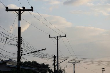 Bulutlu bir gökyüzüne karşı karmaşık elektrik hatları olan çoklu elektrik direkleri, şehir altyapısını ve elektrik dağıtımını gösteriyor.