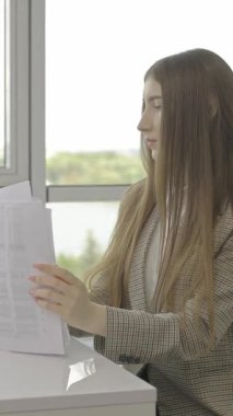 Genç profesyonel kadın masasında oturuyor, dikkatle evrak işlerini hallediyor.